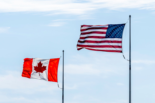 American and Canadian flags with blue sky in background.