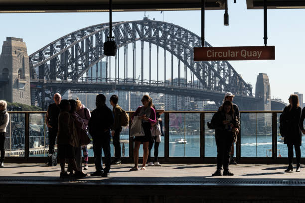 пассажиры ждут своего поезда на станции круговой набережной со знаменитым мостом гавани сиднея на заднем плане. - sydney australia skyline sydney harbor harbor стоковые фото и изображения