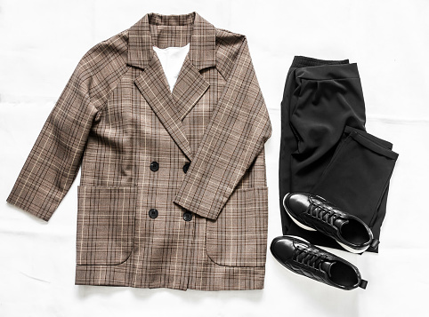 Women's clothing - plaid jacket, black trousers and leather sneakers shoes on a light background, top view