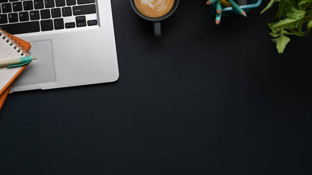 istock Top view of dark workspace with laptop, coffee cup, plant, notebook and copy space on black leather. 1303103126