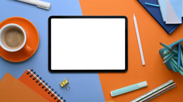istock Top view of digital tablet with empty screen surrounded by designer working tools on two tone blue and orange background. 1303103383