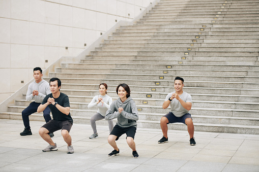 Group of Vietnamese young people training together outdoors and doing squats
