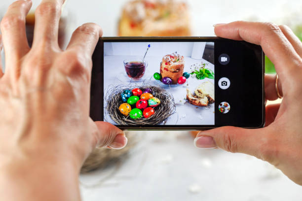 istock Easter cake Kraffin (Cruffin), with nuts and candied fruit sprinkled with powdered sugar, 2021 trend of the easter cake. Top view, female hands take off Easter cake on smartphone. 1303107844
