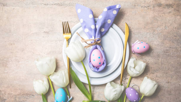 istock Easter holiday table setting with bunny  from egg on white plate and tulips flowers.  Gray concrete table, top view with copy space for text. Happy Easter background 1303109648