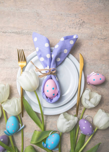 istock Easter holiday table setting with bunny  from egg on white plate and tulips flowers.  Gray concrete table, top view with copy space for text. Happy Easter background 1303109651