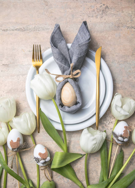 istock Easter holiday table setting with bunny  from egg on white plate and tulips flowers.  Gray concrete table, top view with copy space for text. Happy Easter background 1303109657