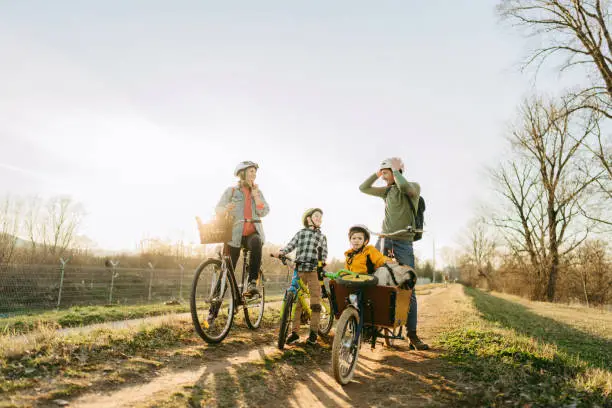 Photo of a cheerful young family with two children who enjoys bicycle ride together, on a sunny springtime day, with their family pet