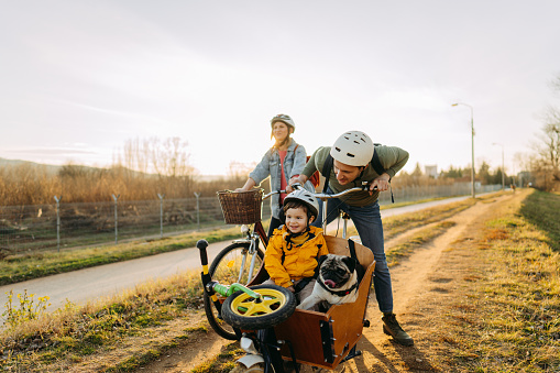 Photo of a cheerful young family who enjoys bicycle ride together, on a sunny springtime day, with their family pet