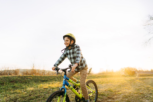 Photo of a smiling young boy riding his bicycle on a beautiful day in nature