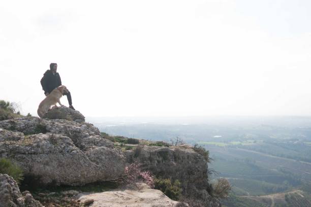 istock Man and dog standing on peak watching the mountain landscape 1303122281