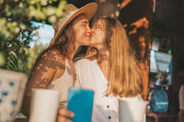 pareja femenina sentada en el café y viendo video por teléfono - parejas monas de lesbianas fotografías e imágenes de stock