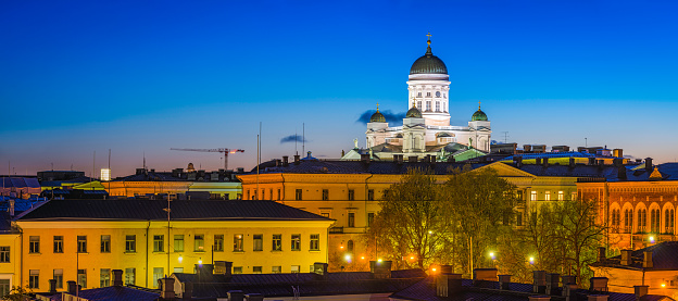 The iconic domes and white towers of Helsinki Cathedral overlooking the Government quarter palaces and offices illuminated under deep blue dusk skies in the heart of central Helsinki, Finland's vibrant capital city.