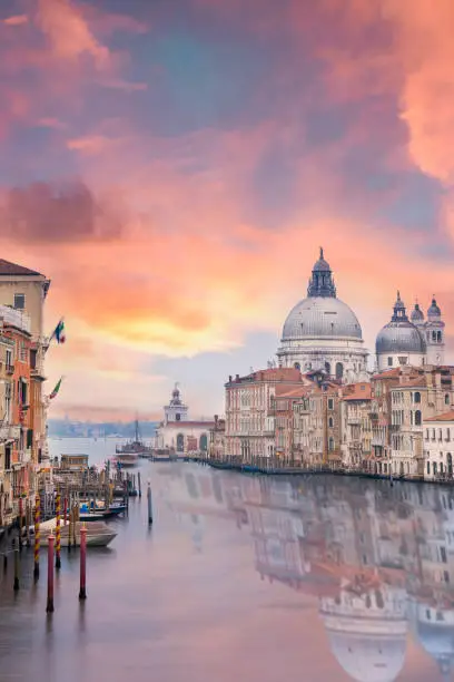 Stunning view of the Venice skyline with the Grand Canal and Basilica Santa Maria Della Salute in the distance during a dramatic sunrise. Picture taken from Ponte Dell’ Accademia, a beautiful wooden bridge. Venice, Italy.