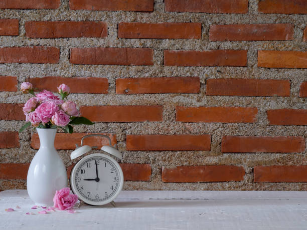 istock Vintage clock with pink roses against brick wall background. 1303125563