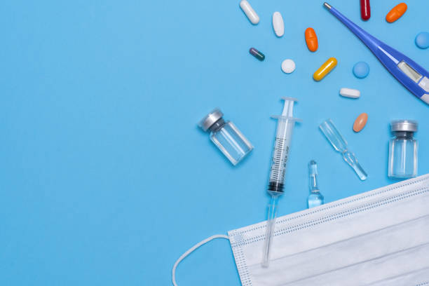 istock Ampoule, vial bottle, syringe under white protective mask and on blue background. Vaccination concept, disease prevention. Health care, Coronavirus vaccine development 1303128157
