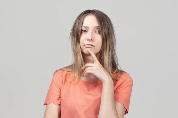 istock Pensive blond girl with thoughtful expression, keeps hand on chin, plans something or makes choice 1303132736
