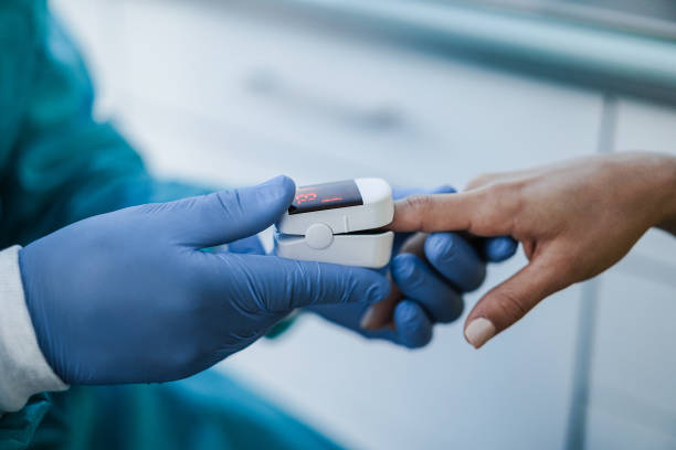 médico que examina al paciente con oxímetro de pulso de yema de los dedos durante el brote de coronavirus - enfoque suave en la mano izquierda - oxímetro de pulso fotografías e imágenes de stock
