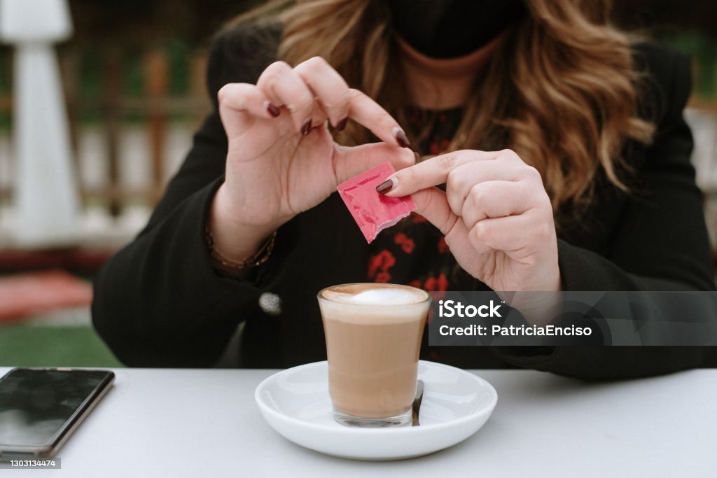 Young woman having a coffee A young woman having a coffee wearing a protective face mask Artificial Sweetener Stock Photo