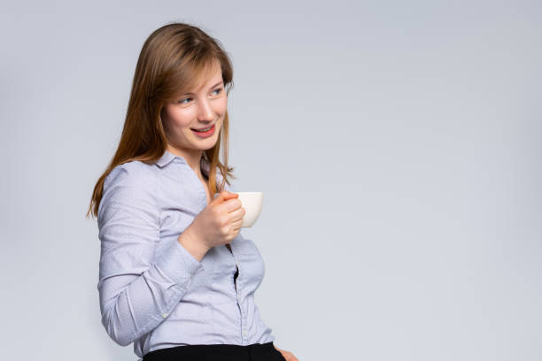 istock Businesswoman agent standing with coffee cup, looking side in distance. Empty space on gray background. Company leader taking break during work day dreaming of success consider investment decision. 1303138149