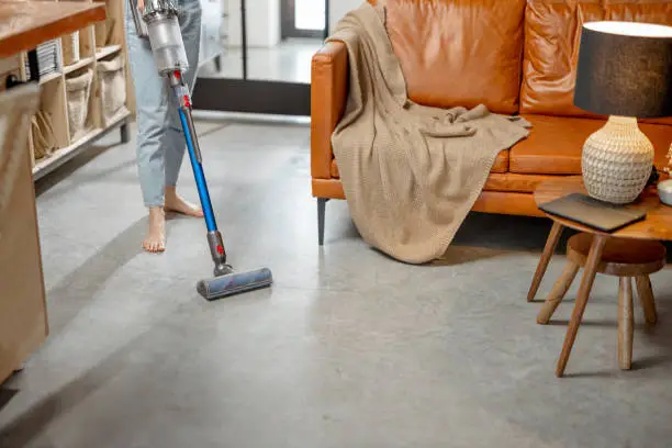 Happy woman with cordless vacuum easy cleaning floor at home in stylish interior design of living room. Smart home concept.