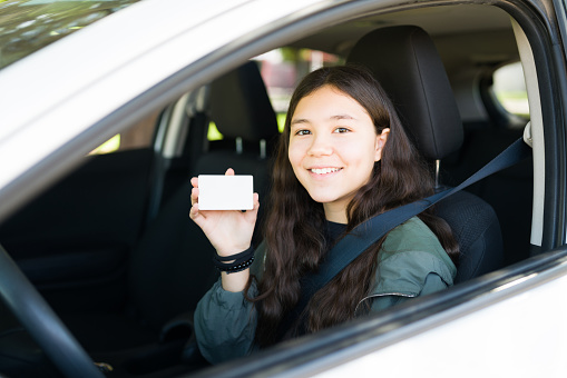 Beautiful teen girl feeling excited to start driving a car and showing her driver's license after passing her test