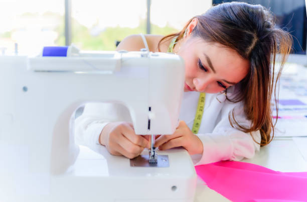 istock Beautiful asian woman tailor and seamstress sews input thread by hand into sewing machine 1303152130