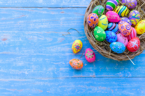 Beautiful colorful easter eggs in wicker basket on blue table wooden with vintage style.