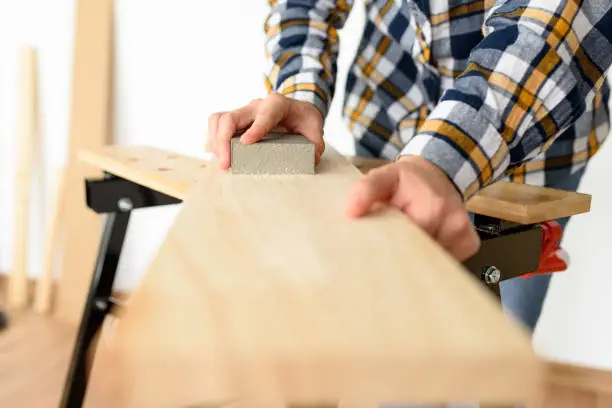 Close-up shot of a woman at home sanding a wood on a workbench. High quality photo.