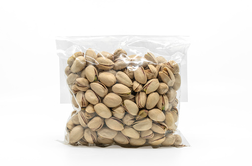 Pistachios in cleared plastic bag packaging for sale on white background. Isolated plastic bag of pistachios with clipping path. Front view, blank space for label branding design.