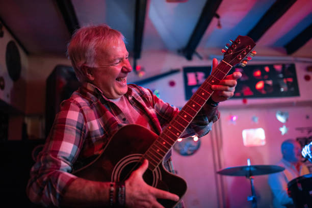 istock Senior man playing guitar on stage with his band 1303156649