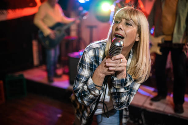 istock Senior woman with a microphone performing on stage with her band 1303156854