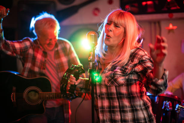 istock Senior woman with a microphone performing on stage with her band 1303156910