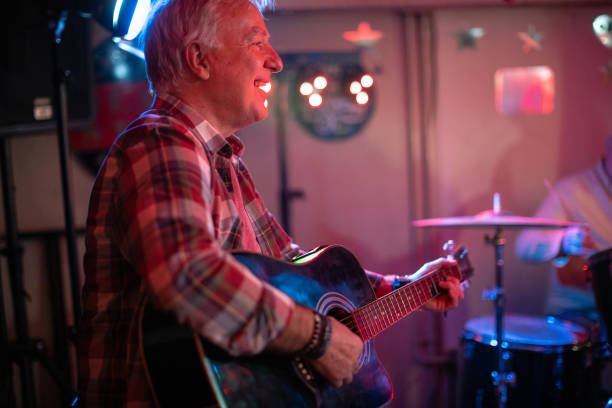 istock Senior man playing guitar on stage with his band 1303156945