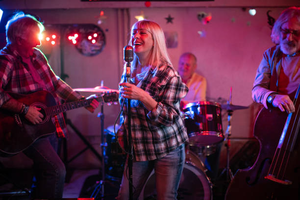 istock Senior woman with a microphone performing on stage with her band 1303156949