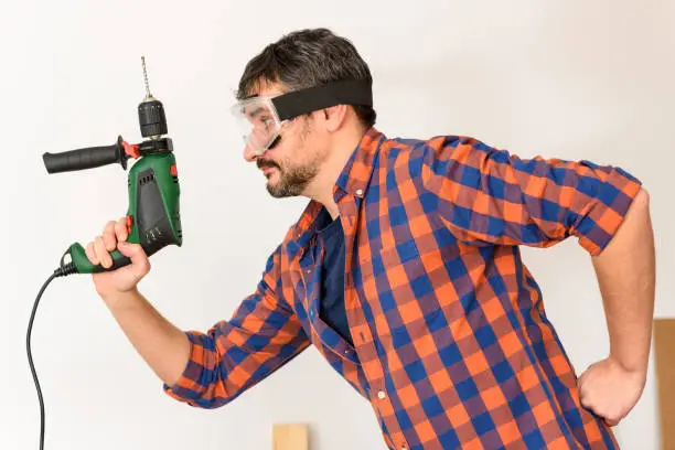 DIY enthusiast man holds a drill. White background. Plain shirt.