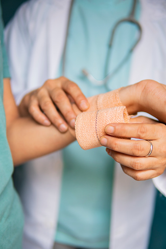 Close-up image of a doctor wrapping bandage on the patient’s wrist.