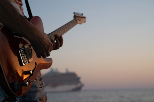 Musician playing electric guitar at sunset, cruise ship in the background
