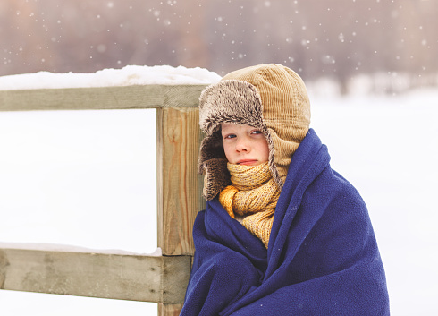 The boy froze in winter and wrapped in a blanket in the winter in the park
