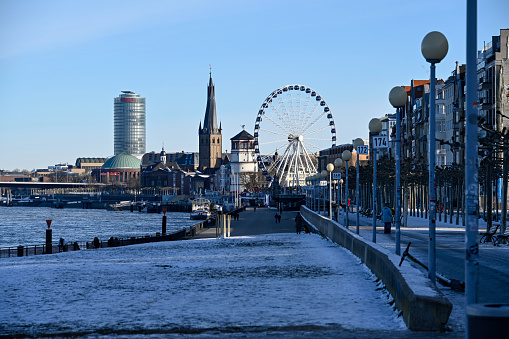 Duesseldorf, Germany, February 14, 2021 - The Rhine embankment promenade in Duesseldorf with Ferris wheels, Schlossturm, Tonhalle  and St. Lambertus Basilica on a snowy winter day.