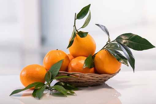fresh orange in a wicker basket with leaves glass on the kitchen table on a light background. selective focus. vitamin and healthy food concept.