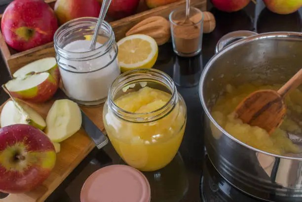 freshly cooked homemade  apple sauce pouring into a jar. Ingredients, cutting board and pot on a stove