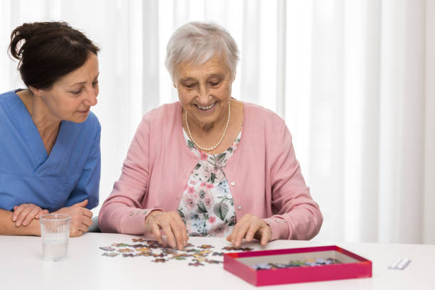 thérapie de maison de soins infirmiers- femme aînée avec le fournisseur de soins - senior adult leisure games playing care photos et images de collection