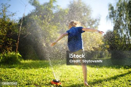 istock Funny little boy playing with garden sprinkler in sunny backyard. Preschooler child laughing, jumping and having fun with spray of water. 1303177242