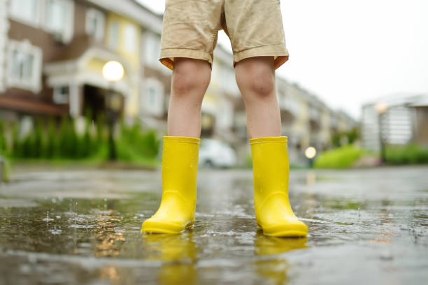 niño con botas de goma amarillas caminando en el día de verano lluvioso en la pequeña ciudad. niño divirtiéndose. juegos para niños bajo la lluvia. - 11681 fotografías e imágenes de stock