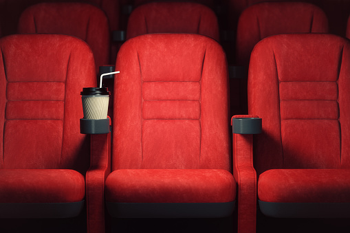 Cinema movie theater concept background. Red cinema seats and coffee or cola paper cup in empty theater.
