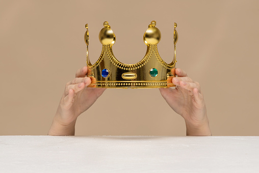 A golden crown in female hands close up above a table.