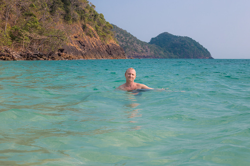 an adult man swims in the sea against the backdrop of mountains in Thailand, on the island of Koh Chang. Summer vacation at sea, travel and tourism.