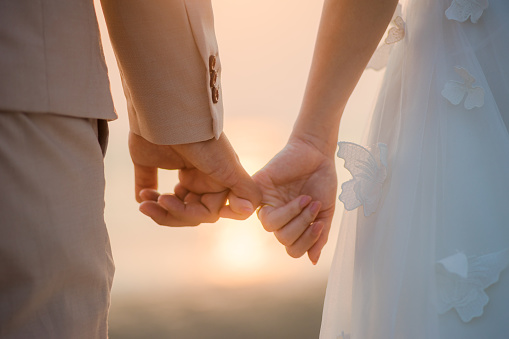 Romantic wedding couple barefoot on pebblestone beach at river on late summer afternoon, groom carrying bride, smiling at each other, full length, copy space