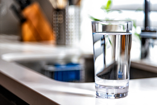 A full glass of drinking water on a kitchen counter near the sink.