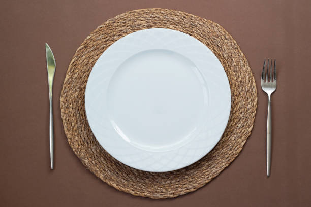 istock Empty white plate on a wicker supla with fork and knife on table. Top view. 1303192512